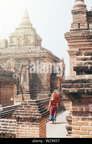 Blonde Caucasian woman with red traditional umbrella stands among the temples and pagodas of ancient Bagan in Myanmar Stock Photo