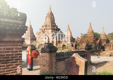 Blonde Caucasian woman with red traditional umbrella stands among the temples and pagodas of ancient Bagan in Myanmar Stock Photo