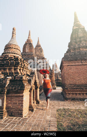 Blonde Caucasian woman with red traditional umbrella runs among the temples and pagodas of ancient Bagan in Myanmar Stock Photo