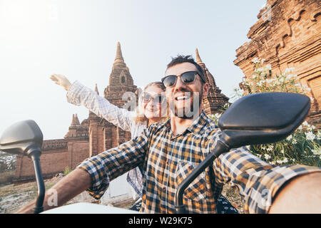Young Caucasian couple making selfie on a motorbike while driving through temples and pagodas of ancient Bagan in Myanmar.
