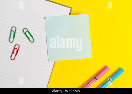 Empty blue paper with copy space paper clips and pencils on the yellow table. Stock Photo