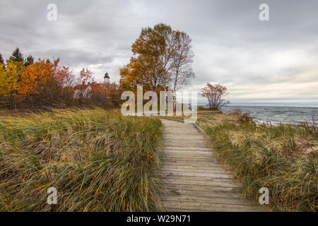 Boardwalk On Beach. Boardwalk trail through dune grass with the Point Iroquois lighthouse along Lake Superior in Hiawatha National Forest of Michigan. Stock Photo