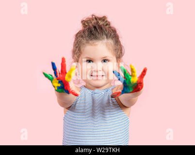 Smiling little girl with hands in the paint on pink background. Stock Photo