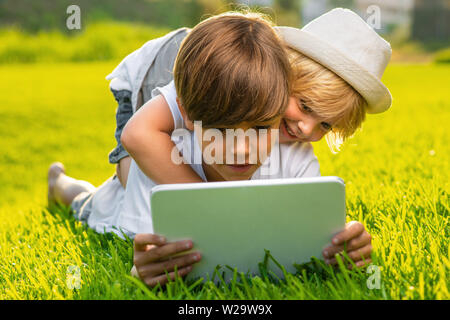 Children look at the tablet lying on the grass Stock Photo