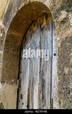 Weathered wooden door with rustic wood grain, rivets and a metal handle in a stone arch frame - angled view, vertical portrait orientation Stock Photo