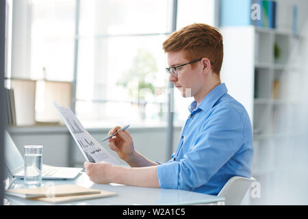 Young banker or financier with papers studying financial charts and graphs Stock Photo