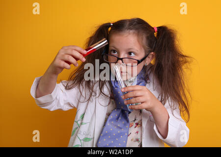 MR - Science Experiment at Home Geek Child in glasses Age 7 - concentrating on pouring mixing liquid chemicals in test tubes on yellow with copy space Stock Photo