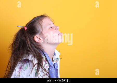 MR - Young little girl / Female Age 7 - child sticking or poking tongue out to right, side view  with copyspace on yellow background Stock Photo