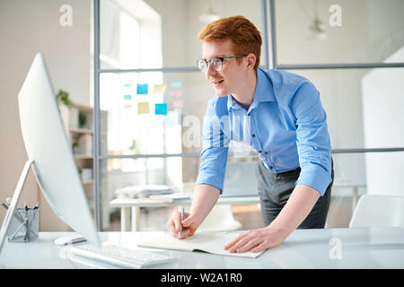 Young programmer making notes while watching video for webdesigners Stock Photo