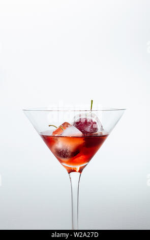 ice cubes with cherries inside into a red cocktail, white background with free space for text Stock Photo