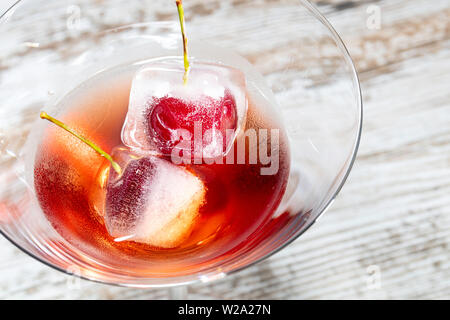 ice cubes with cherries inside into a red cocktail  on a wooden table Stock Photo