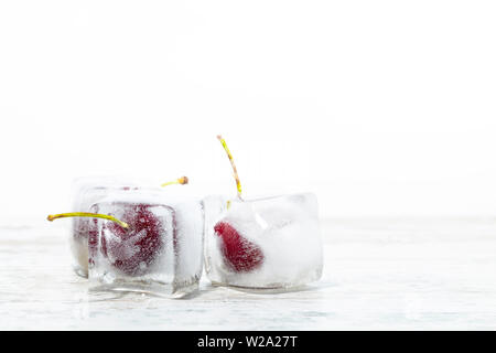 ice cubes with cherries inside on a wooden table and white background with free space for text Stock Photo