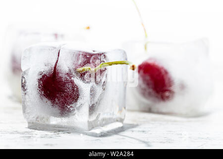 ice cubes with cherries inside on a wooden table and white background Stock Photo