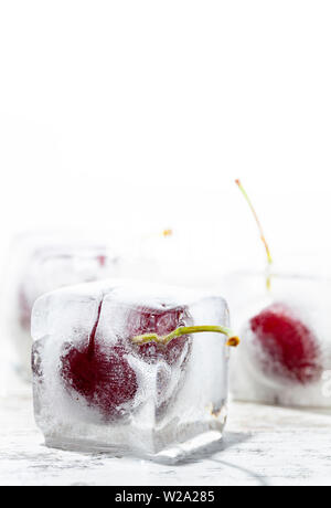 ice cubes with cherries inside on a wooden table and white background Stock Photo