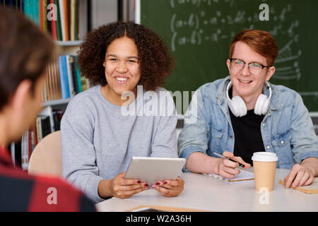 Cheerful girl and her groupmate listening to one of guys during discussion Stock Photo