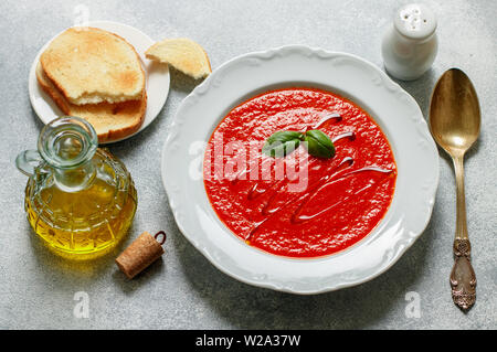 Tomato soup with Basil and spices in a white plate. A thick, hearty dish, served with bread toast and olive oil. Selective focus Stock Photo