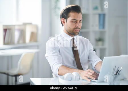 Young serious businessman looking at laptop display by his workplace Stock Photo