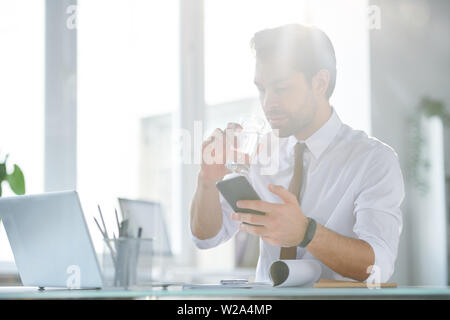 Handsome young businessman with mobile gadget drinking water Stock Photo