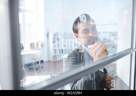 Young coach writing down working notes on transparent board Stock Photo