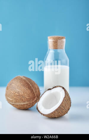 Coconut milk in glass bottle and fresh coconuts with half on blue background Stock Photo