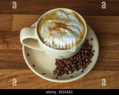 Cappuccino in a Cup with freshly roasted coffee beans on a wooden counter top Stock Photo