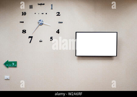 Fire exit sign on wall, fire escape standard sign in building and analog clock and big mornitor with white screen Stock Photo