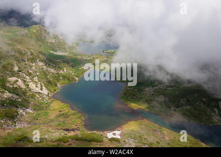 Beautiful light around Twin and Trefoil lakes on Rila mountain and dramatic, thick mist above rocky highlands covered by grass and juniper Stock Photo