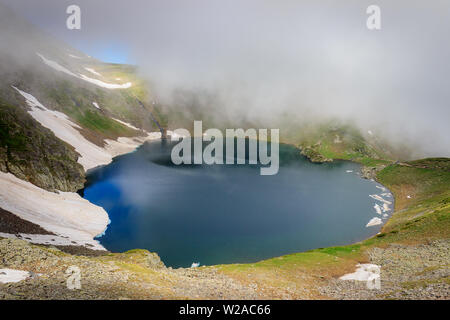 Beautiful misty view of famous the Eye lake on Rila mountain in Bulgaria, sunlit landscape and lots of mountain hikers walking on the highlands Stock Photo
