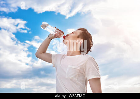 young guy drinks fresh water against of the lake and the forest background. summer thirst. beautiful view Stock Photo