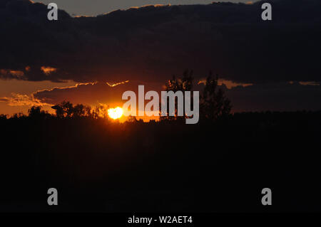Beautiful red sun at sunset. Red sunset sky. The sun is obscured by some clouds at sunset. Big sun in the evening. Heat and hot weather concept. Drama Stock Photo