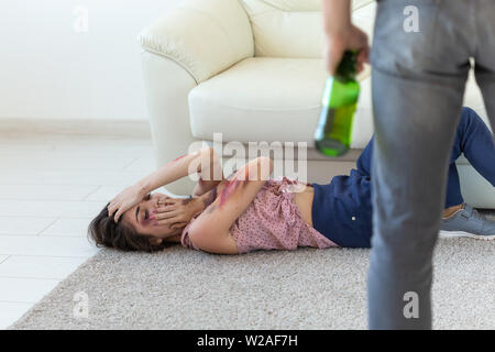 Victim, domestic violence, abuse and alcoholic concept - drunk man with bottle near his wife lying on the floor Stock Photo