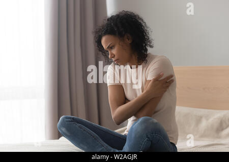 Upset depressed african woman feel sad sit alone on bed Stock Photo