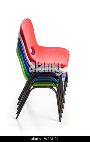 Plastic chairs for children of diverse colors stacked up on a white background, side view. Stock Photo