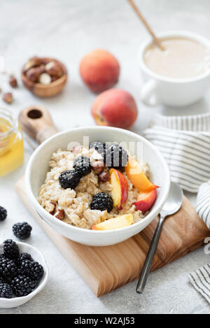 Oatmeal porridge with fruits, berries and honey in a bowl, cup of coffee with milk on background. Healthy breakfast food. Concept of clean eating, die Stock Photo