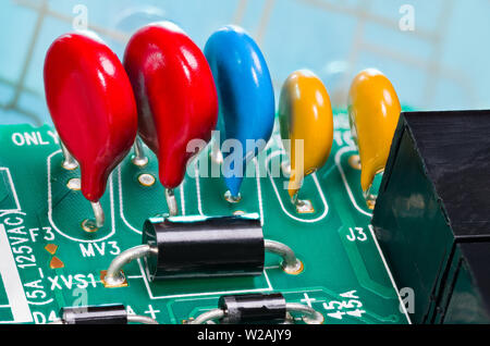 Colorful varistors. Circuit board detail. Electronic components for surge protector. Diode, red, blue, yellow voltage-dependent resistors on green PCB. Stock Photo