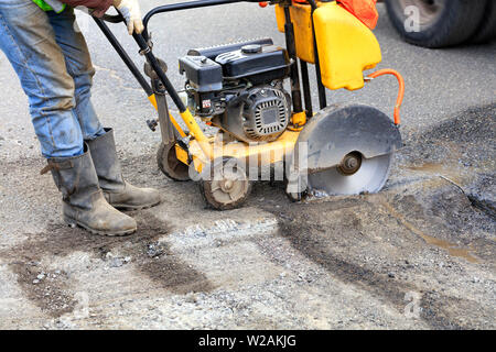 The road technician starts the engine of a gasoline diamond saw to remove old asphalt during repairs on the roadway. Stock Photo