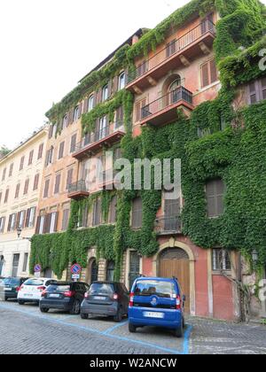 A row of parked cars along the Via di S. Teodoro in front of the ivy-clad, terracotta-coloured buildings in this quiet neighbourhood of Rome. Stock Photo
