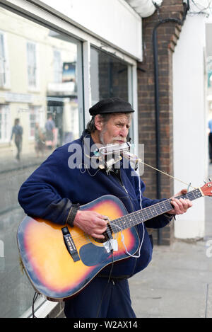 Street Musician playing his guitar and harmonica on the high-street in Wells, Somerset, UK Stock Photo