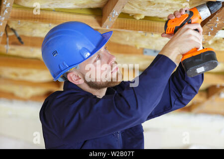 man with drill makes a hole in a wooden ceiling Stock Photo
