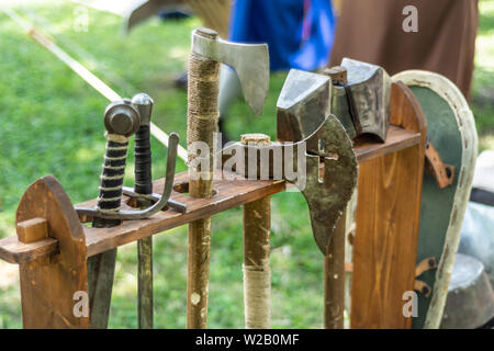 Medieval metal ax and sword in a wooden stand on the festival. Old dark ages weapon and equipment for knights battle. Historical and medieval concept Stock Photo