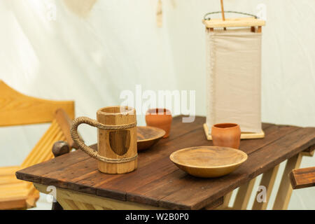 Medieval wooden beer mug and plates on the wooden desk. Very old wooden dishes and bowls for water or alcohol drink and food. Close up Stock Photo