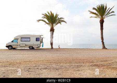 Person walking on beach with mobile caravan near two palm trees Stock Photo