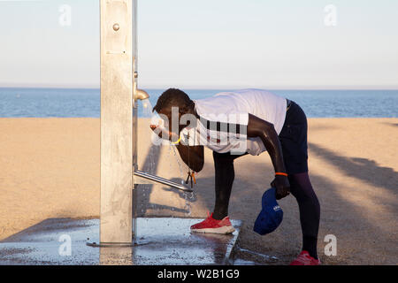 African man drinking water on beach at standpipe Stock Photo