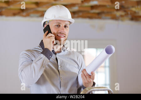 male architect holding rolled up plans and talking on telephone Stock Photo