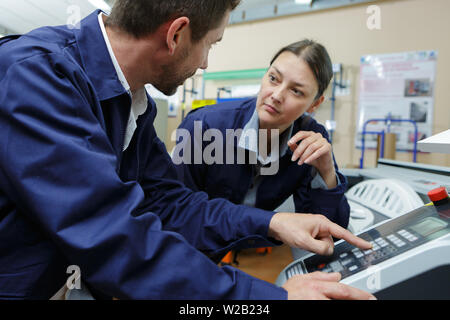 supervisor explaining machinery controls to female worker in factory Stock Photo