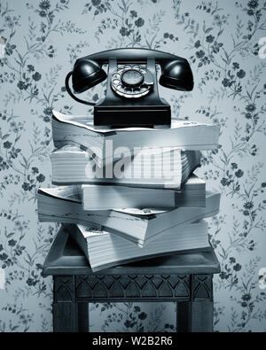 Vintage antique black rotary dial telephone standing on stack of phone books and wooden table Stock Photo