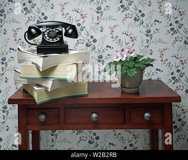 Vintage antique black rotary dial telephone standing on stack of phone books and wooden table with plant Stock Photo