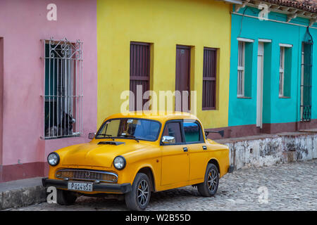 Trinidad, Cuba - June 6, 2019: Old Yellow Car with colorful buildings in the background in a small Cuban Town during a vibrant sunny day. Stock Photo