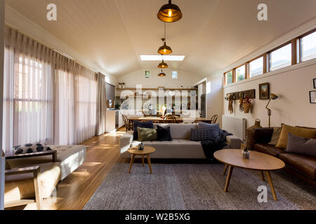 Open plan living, dining and kitchen in a country home with vaulted timber ceiling, highlight windows and sheer curtains Stock Photo