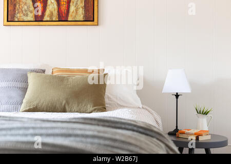 Up close image of bed with green, orange and grey cushions, with books on a bedside table